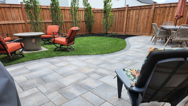 Eine Terrasse mit Steinboden, Gartenmöbeln und einem Holzzaun.