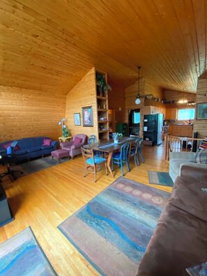 Interior de una cabaña de madera con comedor, sofá y cocina.