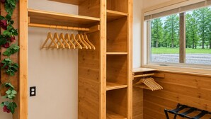 Et træskab med flere hylder og en bøjlestang, et sort tørrestativ og et vindue med udsigt til træer.