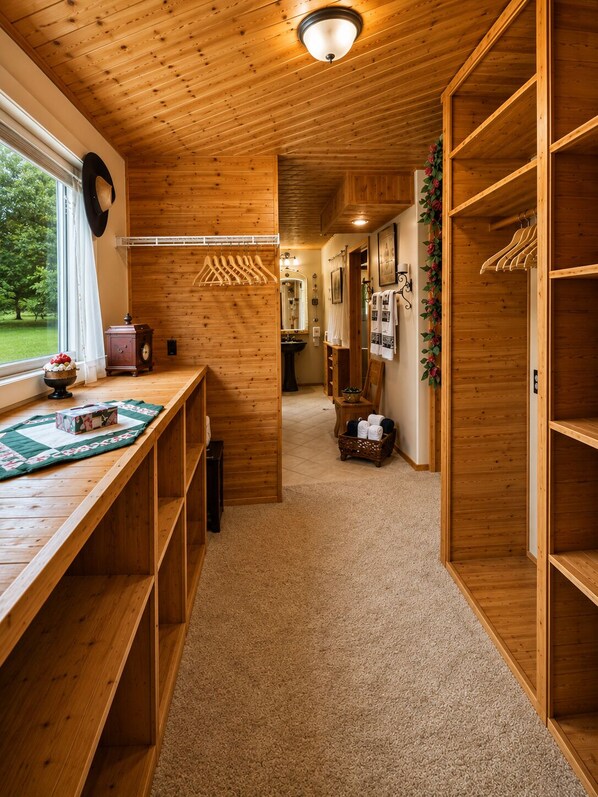 A wooden interior with a hallway leading to a bathroom, a window with curtains, and a wooden bench with a quilt.