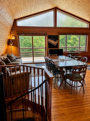 A spacious room with a high ceiling, large windows, a dining table, and a sofa. - Vrbo Members Save 25–27%!. Riverfront. Lake Of the Woods 2mi. Pets Free (Warroad)
