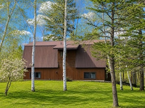 A modern two-story building with a sloped roof, surrounded by a well-maintained lawn and birch trees. - UP TO 25% OFF Members. Riverfront. Lake Of the Woods 2mi. Pets Free (Warroad)