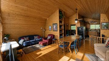 Ein gemütliches Blockhaus-Interieur mit Essbereich, Küche und Wohnzimmer, möbliert mit Holzmöbeln.