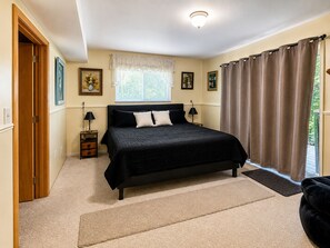 Un dormitorio con cama, mesita de noche, lámpara, ventana con cortinas y puerta.