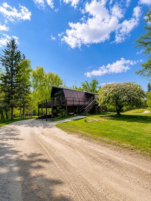 Eine rustikale Holzhütte mit einer Holzterrasse, einer Treppe, die zum Eingang führt, und einem Feldweg, der zum Haus hinaufführt.