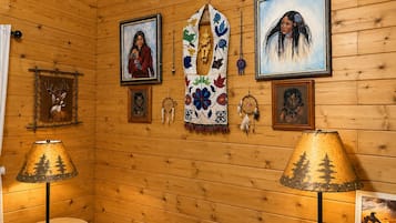 A room with wooden walls, framed artwork, a central woven blanket, and two lamps.