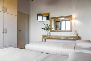A hotel room with two beds, a wooden wardrobe, a mirror, a television, and a bedside table with a lamp.
