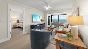 A spacious living room with a large window offering a view of the sea, a ceiling fan, and a cozy seating area with a coffee table. - Mariner Pointe #1021 – Sanibel Waterfront! (Sanibel)