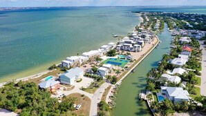 An aerial view of a coastal resort with multiple buildings, a marina, and a clear view of the ocean. - Mariner Pointe #1021 – Sanibel Waterfront! (Sanibel)