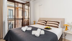 Hotelkamer met een bed, twee kussens, een nachtkastje met een lamp, een dienblad met fruit en uitzicht op het balkon.