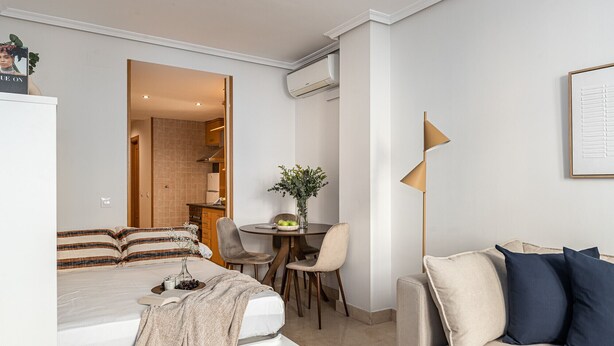 A modern bedroom with a bed, a desk, and a sofa. There is a dining area with chairs and a table. - Waou Gran Via Apartment II - Corta Duració (Madrid)