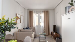A compact living space with a sofa, a coffee table, a TV, and a bookshelf. - Waou Gran Via Apartment II - Corta Duració (Madrid)