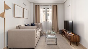 Ein Wohnzimmer mit einer Couch, einem Couchtisch, einem Fernseher und einem Fenster mit Vorhängen.