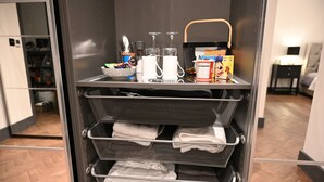 A hotel room with a minibar containing towels, a basket, and a box of chocolates.
