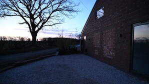 A gravel driveway leading to a brick building with a large window and a tree in the background.