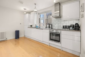 Eine moderne Küche mit weißen Schränken, einem Backofen, einer Kaffeemaschine und einem Fenster für natürliches Licht.