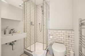 A modern bathroom with a glass-enclosed shower, white subway tiles, a white sink, and a toilet.