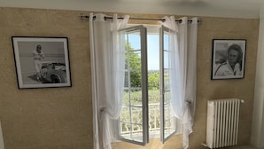 A bedroom with a bed, a window with curtains, a radiator, and two framed pictures on the wall.