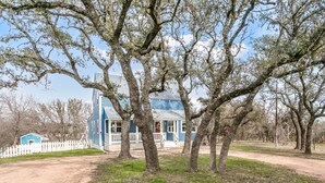 Une maison bleue avec un porche, entourée d’arbres.