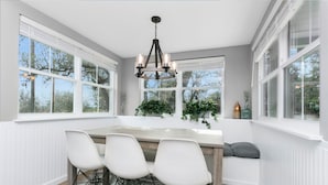 Un coin repas avec une table en bois, quatre chaises blanches et un lustre.