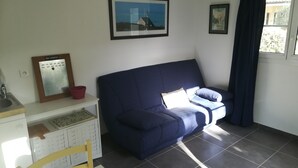 A room with a blue sofa, a small table with a red basket, a framed calendar, and a window with curtains.