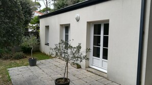 A building with a white exterior, a small garden with potted plants, and a paved patio area.