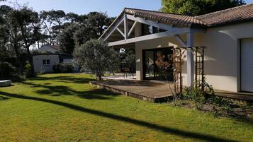 Une maison moderne dotée d’une grande terrasse, entourée d’une pelouse bien entretenue et d’arbres.