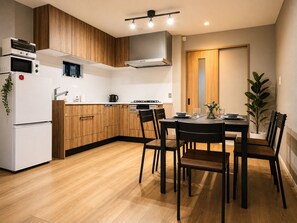 A modern kitchen with wooden cabinets, a white refrigerator, and a dining area with a table and chairs. - Direct access to Osaka Kansai Airport,5 minutes by train from Nanba (Nishinari-ku, Osaka)