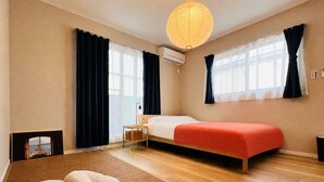 Ein Schlafzimmer mit einem Bett, zwei mit Vorhängen versehenen Fenstern, einer Hängelampe, einem Nachttisch und einem Teppich.