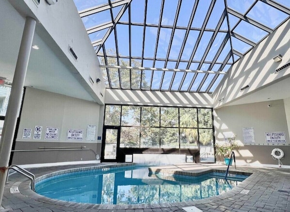 An indoor swimming pool with a glass ceiling, surrounded by walls with safety signs.