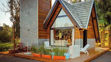 A modern house with a large glass window, wooden deck, and outdoor seating.