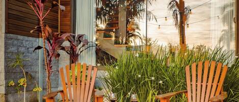 A fire pit with two wooden chairs and a table, surrounded by plants and a brick floor.