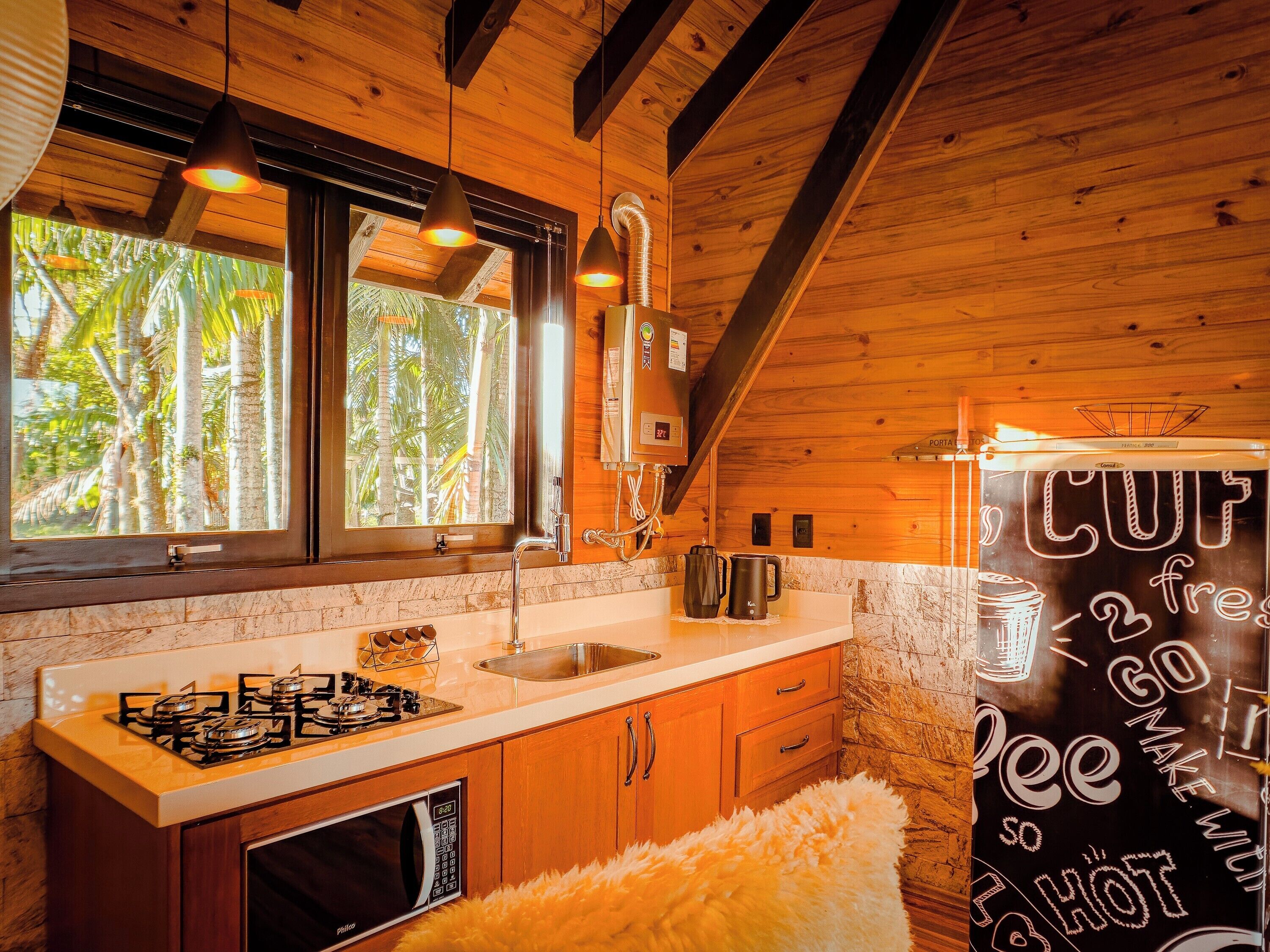 Una cocina con armarios de madera, una estufa a gas, un fregadero y una ventana con vistas a palmeras.