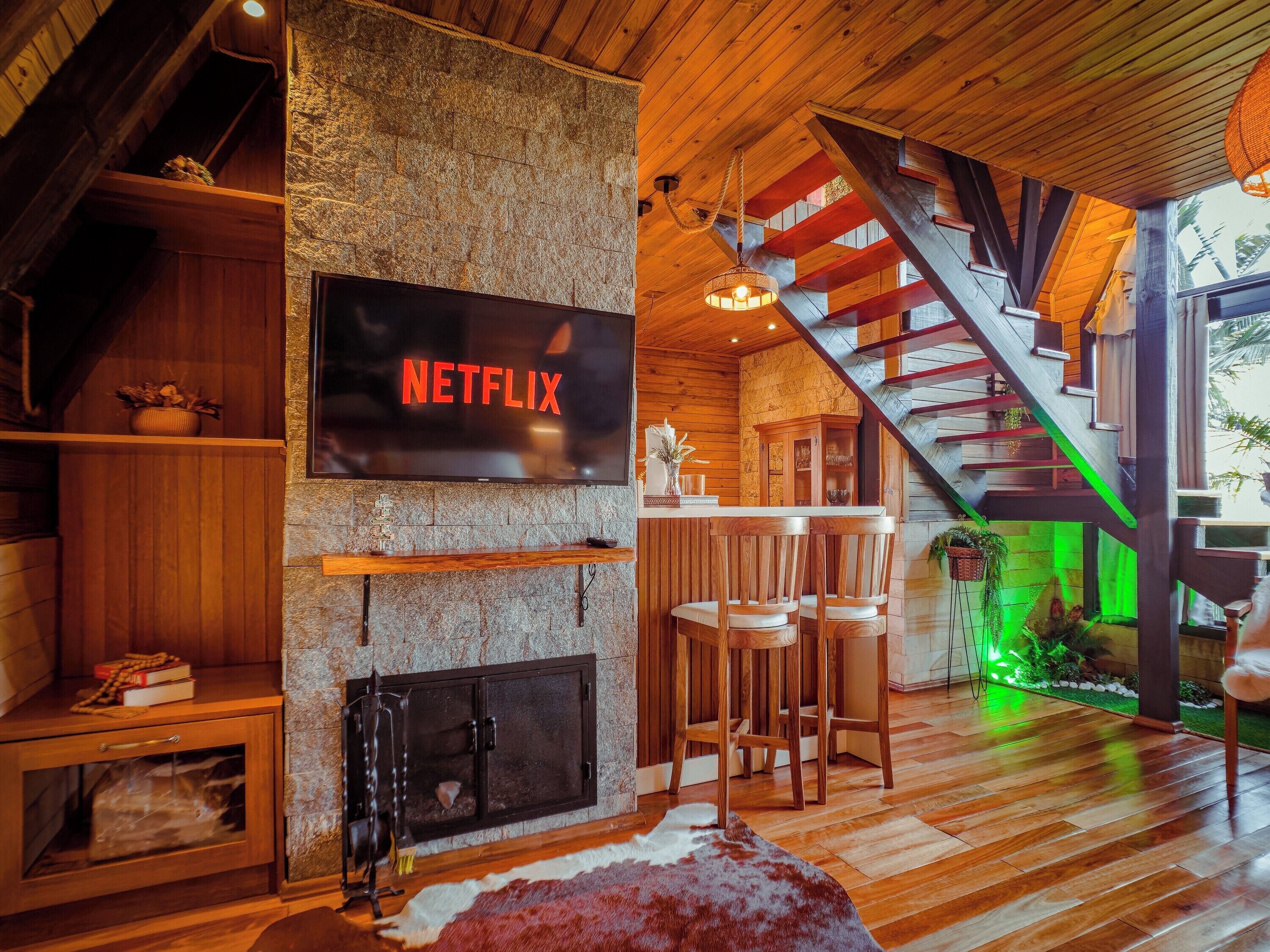 A cozy interior with a stone wall, wooden furniture, a fireplace, and a staircase.
