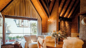 A cozy room with a wooden ceiling, a sofa, a dining table with chairs, and a vase of flowers. - AriMara Chalés & Ecoturismo (Mampituba)