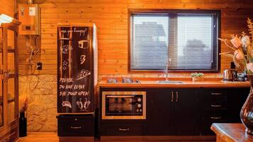 Un intérieur en bois avec une cuisine équipée d’un four encastré, un tableau noir portant un message et une fenêtre avec des stores.