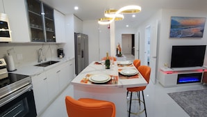 Een moderne keuken met een centraal eiland, witte kasten en oranje stoelen.