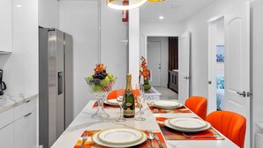 Een moderne eetruimte met een lange tafel, gedekt voor een maaltijd, een koelkast en een decoratieve lamp.