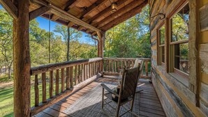 A wooden cabin with a porch, a rocking chair, and a view of the surrounding forest. - Secluded Log Cabin Near Hot Springs-Pet Friendly (Hot Springs)