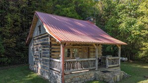 A rustic log cabin with a metal roof, stone foundation, and a porch with a railing. - Secluded Log Cabin Near Hot Springs-Pet Friendly (Hot Springs)
