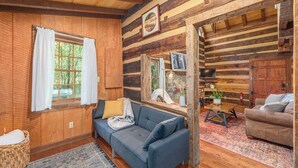 A cozy log cabin interior with a blue sofa, a wooden dining table, and a stone fireplace. - Secluded Log Cabin Near Hot Springs-Pet Friendly (Hot Springs)