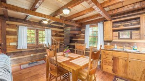 A rustic cabin interior with a wooden dining table, chairs, a kitchen area, and a staircase. - Secluded Log Cabin Near Hot Springs-Pet Friendly (Hot Springs)