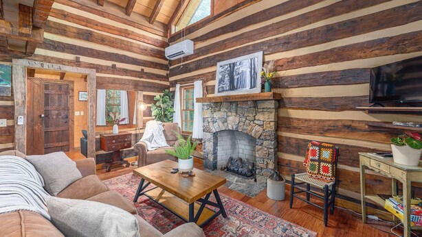 A log cabin interior with a stone fireplace, wooden walls, a sofa, a coffee table, and a television. - Secluded Log Cabin Near Hot Springs-Pet Friendly (Hot Springs)
