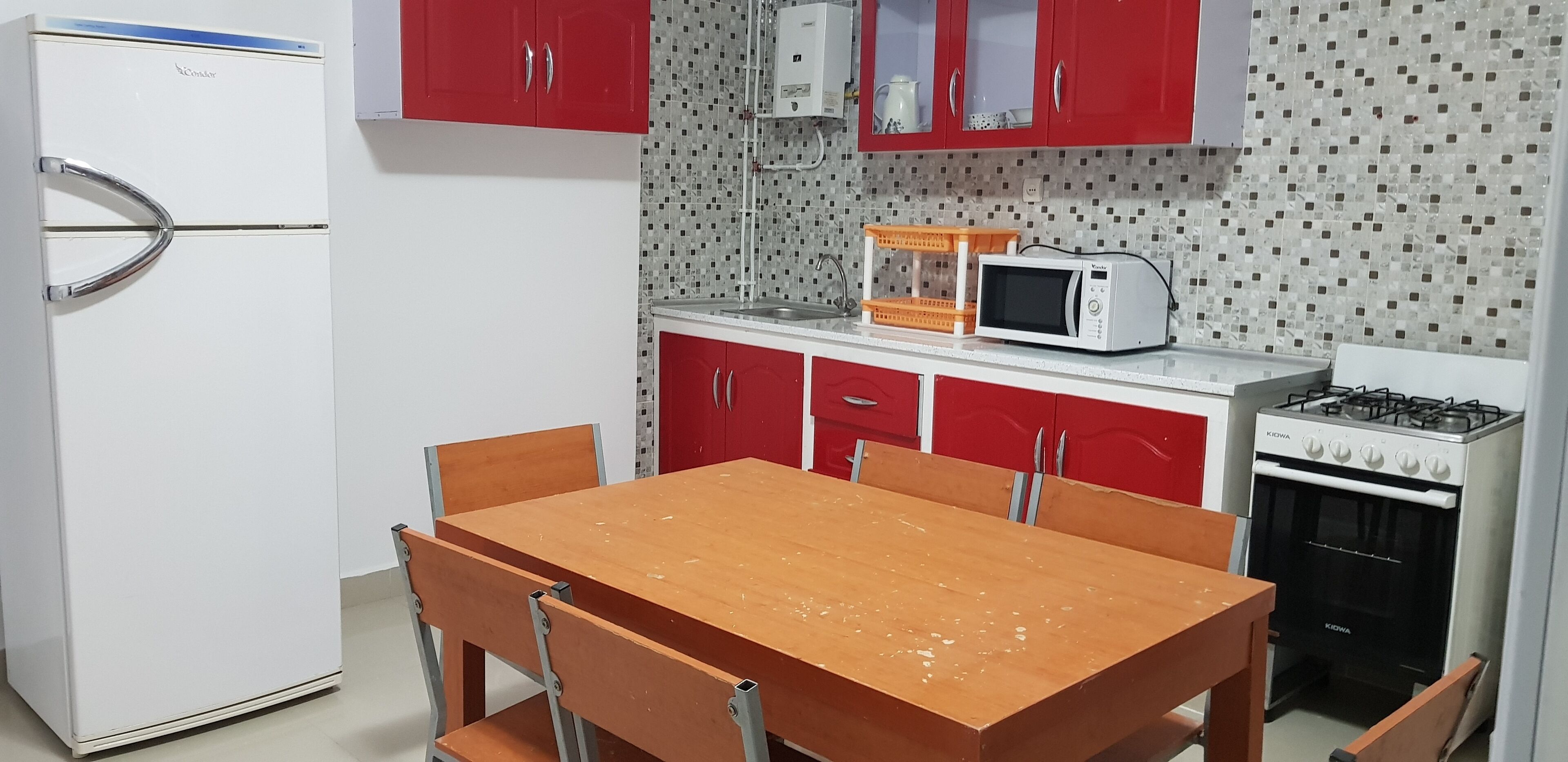 A compact kitchen with a white refrigerator, red cabinets, a wooden dining table, and a gas stove.