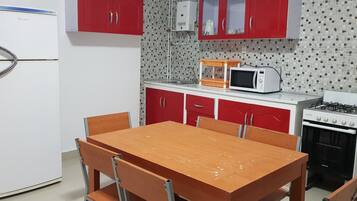 A compact kitchen with a white refrigerator, red cabinets, a wooden dining table, and a gas stove.