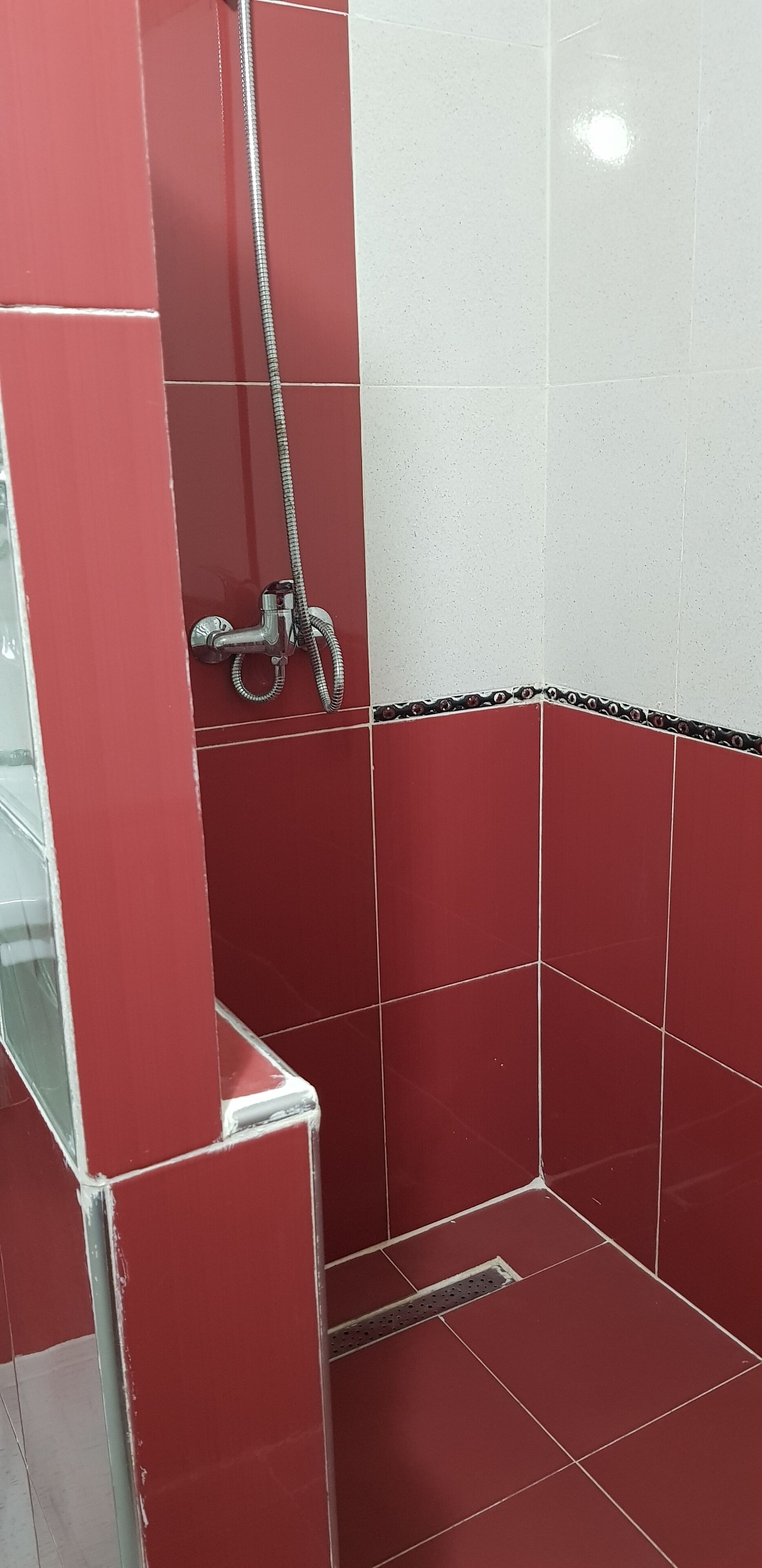 Un espacio de ducha con azulejos rojos y blancos, un cabezal de ducha y un desagüe.