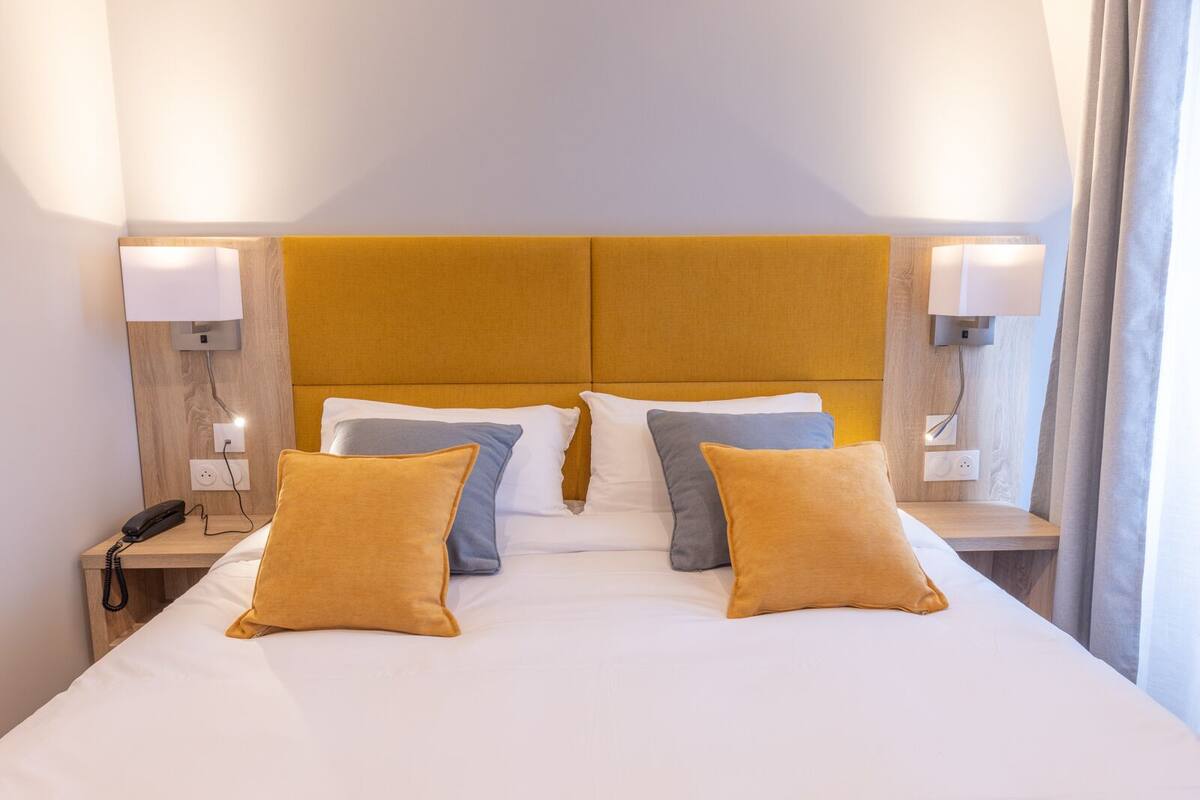 Quarto de hotel com uma cama grande, duas mesas de cabeceira, um telefone e luminárias fixadas na parede.