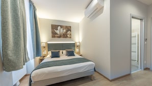 A neatly arranged bedroom with a bed, bedside lamps, an air conditioning unit, and a door leading to another room. - HOTEL SAINT AUGUSTIN (Strasbourg)