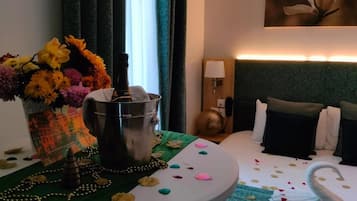 A hotel room with a bed, a nightstand with a lamp, a vase of flowers, and a bottle of champagne.