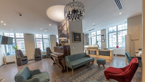 A spacious living room with a piano, sofas, and a chandelier. - HOTEL SAINT AUGUSTIN (Strasbourg)